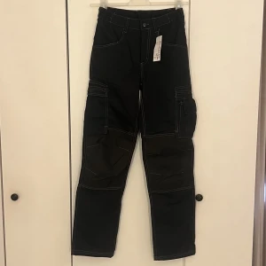 Arbetsbyxor från Jula  - Säljer ett par svarta arbetsbyxor från jula med vita kontrastsömmar och flera praktiska fickor på sidorna och ibak. Byxorna har förstärkta partier på knäna och en rak passform. Endast testade. 