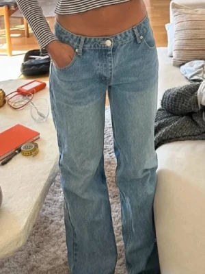 Blåa raka jeans med low- mid vaist - Säljer ett par ljusblå jeans med rak passforma. Jeansen har klassisk femficksdesign, knappgylf och är tillverkade i denim. Perfekta till en avslappnad och trendig look.