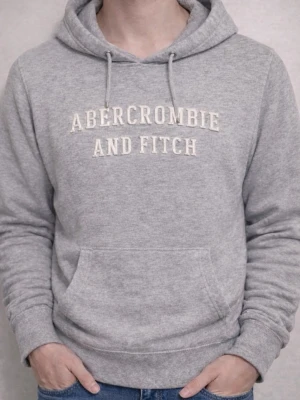 Grå hoodie från Abercrombie & Fitch - Snygg grå hoodie från Abercrombie & Fitch med broderad logga på bröstet. Klassisk känguruficka framtill och justerbar huva med dragsko. Tillverkad i mjukt material som känns skönt mot huden. Perfekt för en avslappnad och trendig look.