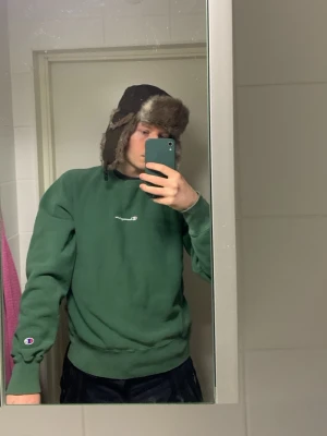 Grön sweatshirt från Champion - Snygg grön sweatshirt från Champion med broderad logga på bröstet. Klassisk rund halsringning och ribbade muddar vid ärmslut och nederkant. Perfekt för en avslappnad och sportig stil.      Det står storlek S på den men skulle säga att den passar mer storlek Medium