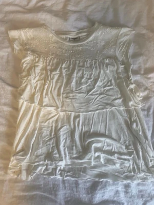 Vit blus med spets från Kappahl - Söt vit blus från Kappahl med korta ärmar och dekorativ spets upptill. Blusen har ett lätt och luftigt tyg med volangdetaljer och rund halsringning. I storlek 170 men sitter som XS/S. Använd få gånger, liten fläck på ryggen men inget som snys.