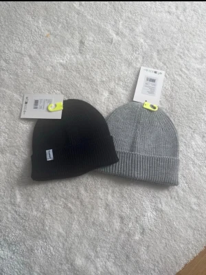 Svart ribbstickad mössa från Craft - Säljer en svart och grå  ribbstickad mössor från Craft med uppvikt kant och diskret logotypmärke på sidan. Klassisk modell i mjukt material som sitter skönt på huvudet. Perfekt för kalla dagar och enkel att matcha med olika outfits.