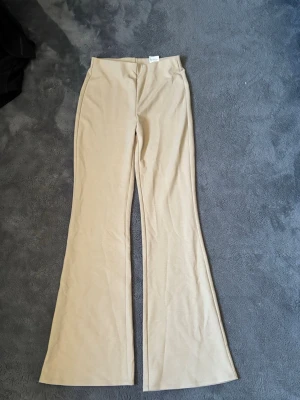 Beiga utsvängda leggings från H&M - Säljer ett par beiga leggings från H&M i storlek S. De har en utsvängd passform  och är tillverkade i ett mjukt stretchigt material. Perfekta för en avslappnad och trendig look.