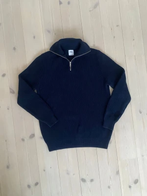 Mörkblå stickad tröja från Zara - Snygg mörkblå stickad tröja från Zara med halv dragkedja och hög krage. Tröjan har ribbstickad struktur och långa ärmar. Perfekt för lager på lager och enkel att matcha med jeans eller byxor.