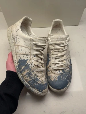 Maison margiela paint splatter  - Unika maison margiela gats med blått färgstänk över hela skon. Lågt skaft och klassisk snörning. Tillverkade i läder med en vintage-inspirerad look och detaljerade sömmar. Perfekta för dig som vill sticka ut med din stil.