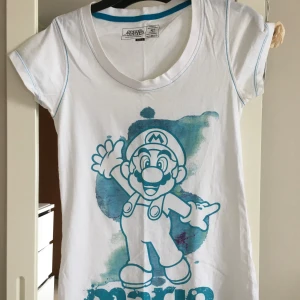 Vit Super Mario t-shirt - vintage Säljer en supercool vit t-shirt med ett stort tryck av Super Mario i blått. T-shirten är i bomull och har korta ärmar. Perfekt för alla Mario-fans! 🕹️