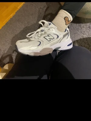 Vita New Balance 530 sneakers - Säljer ett par vita New Balance 530 sneakers med mesh och syntetdetaljer. Skorna har blå och silverfärgade inslag, klassisk N-logga på sidan och chunky sula. Perfekta för dig som gillar retrostil och bekväma skor.