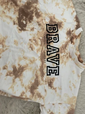 Tie-dye  t - shirt  med BRAVE-tryck - Säljer en snygg  t-shirt  i vitt och brunt tie-dye-mönster med stort BRAVE-tryck på bröstet och texten 'Brilliant Future' under.