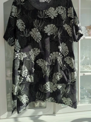 Svart blommig tunika från Isolde - Svart kortklänning/ tunika från Isolde med ljusgrönt blommönster. Klänningen har korta ärmar, rund halsringning och två fickor framtill med knappdetalj. Perfekt för dig som gillar en avslappnad och bekväm stil.