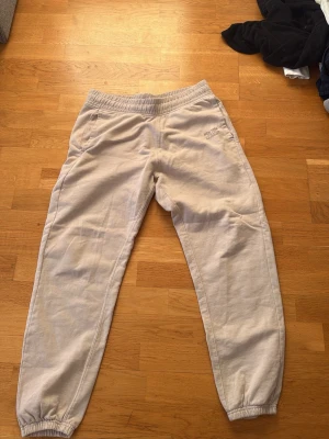 Beige mjukisbyxor New Balance - Säljer ett par beige mjukisbyxor från New Balance med resår i midjan och vid bensluten. Byxorna har en avslappnad passform och är tillverkade i mjukt material, perfekta för chill dagar. Diskret logga på vänster sida. Supersköna och stilrena!