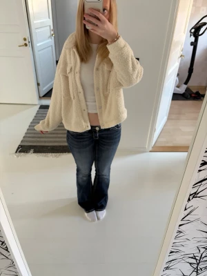 Beige teddy cardiganjacka - Mysig beige teddy cardiganjacka med krage och knappar framtill. Jackan har en avslappnad passform och två bröstfickor. Perfekt för lager på lager och ger en trendig look till din outfit.                   Fåtal gånger använd och är i bra stick!💕.                    Köpt från yunkjard i märket Urban classics