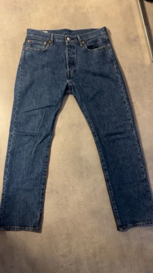 Levi's 501 - Klassiska blå jeans från Levi's med rak passform och fem fickor. Jeansen har en knappgylf, den ikoniska läderlappen bak i midjan. Tillverkade i slitstark denim med en tidlös look som funkar till allt. W33 L32