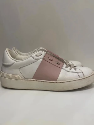 Valentino open - Snygga sneakers i vitt läder med en bred rosa panel på sidan och nitar vid hälen. Klassisk låg modell med vita och rosa detaljer samt platt sula. Perfekta för dig som gillar stilrena men ändå unika skor.