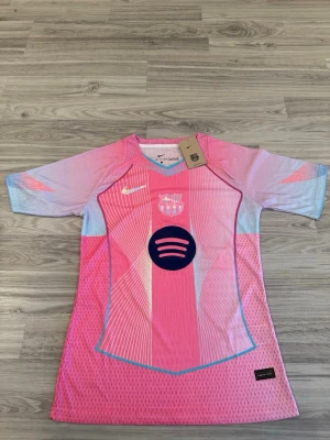 Barça x Nike rosa matchtröja - Säljer en limited edition FC Barcelona matchtröja från Nike i rosa och ljusblå toner. Tröjan har korta ärmar, klubbmärke och Nike-logga på bröstet samt Spotify-logga i mitten. Tillverkad i ett lätt och ventilerande funktionsmaterial, perfekt för fotbollsplanen.