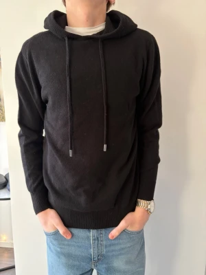 100% Merinoull Stickad Hoodie - Bengtson’s Merino | Helt Ny | Noir | 100% Merinoull | Storlek S | Modellen är 178 | Snören går att korta ner!
