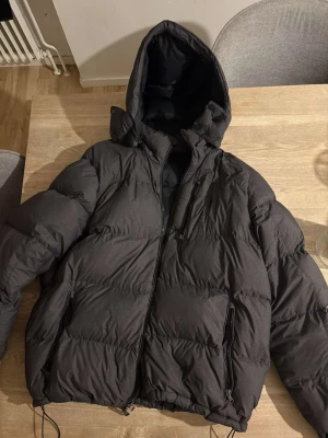 Ralph lauren jacka - Säljer en mörk grå pufferjacka från Polo Ralph Lauren med huva och dragkedja framtill. Jackan har två sidofickor med dragkedja och en bröstficka med dragkedja. Klassisk broderad logga på bröstet. Perfekt för kalla vinterdagar.