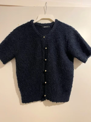 Mörkblå kortärmad kofta från Gina Tricot - Mörkblå kofta från Gina Tricot med korta ärmar och rund hals. Koftan är en fluffig och varm. Inga skador eller fläckar på den. Sällan använd.