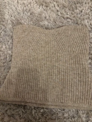 Beige ribbad stickad tubtopp - Säljer en beige ribbad stickad tubtopp i mjukt material. Toppen är axelbandslös och har en lätt croppad passform som sitter snyggt. Perfekt att styla med höga jeans eller kjol för en trendig look. Storleken är med som S hade ja sagt själv. Säljs på vinted också