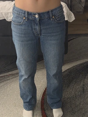 Blå raka jeans med låg midja - Säljer ett par klassiska blå jeans med rak passform och låg midja. Jeansen har fem fickor, bälteshällor och stängs med knapp och dragkedja. Tillverkade i kraftigt denimtyg som ger en tidlös look. Perfekta till sneakers eller boots.