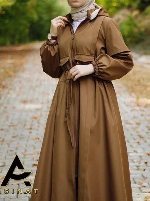 Brun lång rock med huva från Asinat - Snygg brun lång rock från Asinat med dragkedja framtill, justerbar midja med knytband och två stora fickor. Rocken har en huva med ljus foderkant och elastiska muddar vid ärmsluten. Perfekt för dig som gillar modestil och vill ha en stilren look.