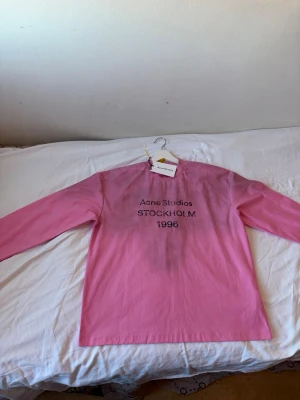 Rosa långärmad tröja Acne Studios - Trendig rosa långärmad tröja från Acne Studios med tryck 'STOCKHOLM 1996' på bröstet. Perfekt för dig som gillar stilrena och coola plagg med en touch av streetwear. Rund halsringning och avslappnad passform.