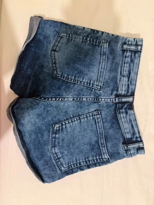 Blå denimshorts från Divided - Säljer ett par klassiska blå denimshorts från Divided. Shortsen har hög midja, två stora bakfickor och en snygg tvättad look. Perfekta för varma dagar och enkla att matcha med olika toppar.