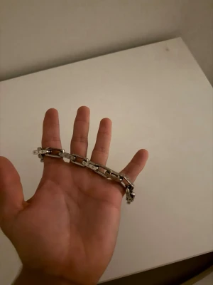 Silverfärgat länkarmband - Stilrent armband i silverfärg med rejäla länkar och detaljerade mönster på varje länk. Armbandet har en modern och edgy känsla, perfekt för att lyfta vilken outfit som helst. Länkarna är fyrkantiga och ger ett robust intryck.