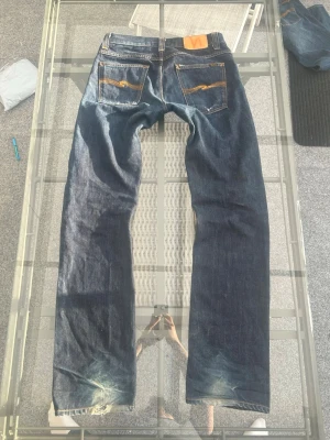 Nudie Jeans W32/L36 – mörkblå denim, 100% bomull - Säljer ett par riktigt snygga Nudie Jeans i modellen Average Joe Dark Oldie, storlek W32/L36. Mörkblå denim i 100% bomull med klassisk rak passform som sitter bra och fungerar till allt från streetwear till clean och vintage outfits. Fina detaljer, snygg tvätt och naturlig fading som ger jeansen karaktär. Bra skick och perfekta för dig som gillar kvalitetsdenim med tidlös stil.