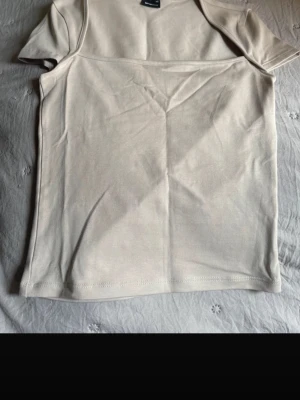 Beige kortärmad t-shirt - Säljer en enkel och stilren beige t-shirt från Monki. T-shirten har korta ärmar och en rak passform, perfekt till alla typer av outfits. Tillverkad i mjuk bomull för skön känsla hela dagen.