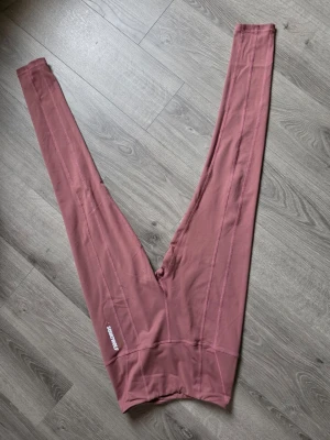MörkRosa leggings från Squat Wolf - Säljer ett par snygga rosa träningsbyxor från Squat wolf med hög midja och långa ben. De har synliga sömmar och logga på ena benet. Materialet är stretchigt och passar perfekt till träning eller chill. Superskön passform och trendig färg!