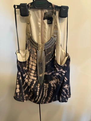 Mönstrad linnetopp från H&M - Cool linnetopp från H&M med batikinspirerat mönster i svart och beige. Toppen har djup ringning och smala axelband. Materialet känns mjukt och lätt, perfekt för varma dagar. Snyggt detaljerad med en dekorativ guldfärgad kedja framtill.