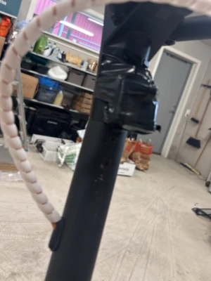 Svart elsparkcykel med spiralhölje -  Navve Elsparkcykel i svart med spiralformat vitt kabelskydd längs styret. Handtagen är grå och styret har en digital display. Konstruktionen är mestadels i metall och plast. Perfekt för smidig transport i stan. Info om hastighet kan ni skriva om