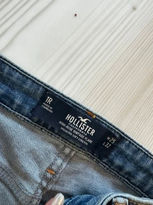 Hollister high-rise flare jeans blå - Snygga blå high-rise vintage flare jeans från Hollister med slitningar på knäna. Modellen har utsvängda ben och klassisk femficksdesign. 