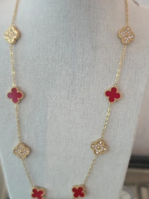 Guldhalsband med röda och pärlprydda klöver - Långt halsband i guldton med klöverformade hängen, varav några är röda och andra dekorerade med små pärlor. Kedjan är tunn och elegant, och klöverhänget ger en trendig och lyxig känsla. Perfekt för att lyfta vilken outfit som helst.