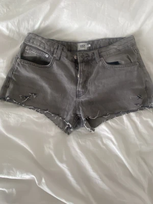 Grå denimshorts med rå kant - Säljer ett par grå denimshorts från 157 med rå och fransig kant. Från början vara det ett par icon jeans från lager157 som jag klippte av❣️