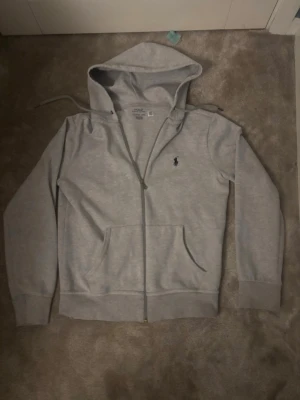 Ralph lauren zip hoodie  - Ralph Lauren zip hoodie i grå färg säljes. Storlek XS. Bra skick och väldigt skön hoodie med klassisk passform och dragkedja framtill. Perfekt till vardag och lätt att matcha med olika outfits. Utmärkt skick då jag endast använt den 1 gång för den var för liten!  Pris: 299 kr