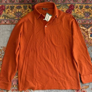 Loro Piana Piqué  - Snygg rostorange långärmad skjorta med klassisk krage och knappar framtill. Skjortan är tillverkad i ett strukturerat bomullstyg som ger en cool och avslappnad känsla. Perfekt för dig som vill sticka ut med färg och stil. Sprillans ny.