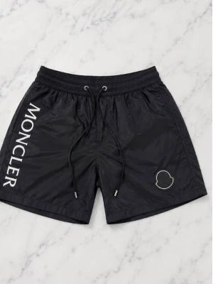 Svarta shorts från Moncler - Snygga svarta badbyxor från Moncler med vit logotyp längs ena benet och broderad Moncler-patch. De har elastisk midja med dragsko och är tillverkade i ett lätt, snabbtorkande material. Perfekta för stranden eller poolen.