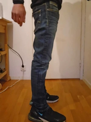 Replay herr W29 L32 - Snygga blå slim fit jeans från Replay med klassisk femficksdesign och diskreta slitningar. Jeansen har dragkedjegylf och tydliga kontrastsömmar. Perfekta för dig som gillar en smal passform och stilren look.