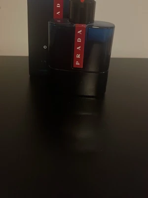 Prada Luna Rossa ocean - Säljer en Prada Luna Rossa Black parfym i en elegant svart flaska med röd detalj och tydlig Prada-logga. Flaskan har en modern, stilren design och är tillverkad i glas med plastlock. Perfekt för dig som gillar exklusiva dofter.