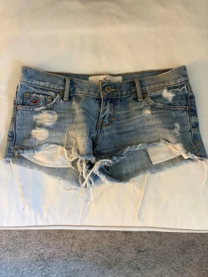 Ljusblå slitna low waist jeansshorts Hollister - Säljer ett par låg midjade ljusblå jeansshorts från Hollister med slitna detaljer, fransig kant och klassisk femficksmodell. Shortsen har låg midja. Perfekta för en avslappnad och trendig sommarstil. 