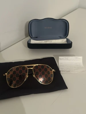 Gucci aviator solglasögon guld - Snygga aviator solglasögon från Gucci med guldfärgade metallbågar och mörka linser. Linserna har ett tydligt Gucci-mönster i guld över hela ytan. Klassisk och trendig design som sticker ut.Finns även kvitto.