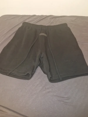 Svarta shorts från Essentials - Svarta shorts från Essentials med elastisk midja och diskret logga broderad på vänster ben. Tillverkade i mjukt material, perfekta för chill eller träning. Klassisk passform med snörning i midjan för extra komfort.