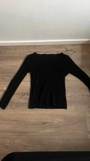 Svart ribbad långärmad tröja - Säljer en svart, ribbad långärmad tröja med smal passform och V-ringning. Tröjan har en enkel och stilren design som passar till det mesta. Materialet ser ut att vara stretchigt och mjukt, perfekt för en trendig vardagslook.