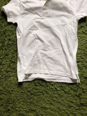 Vit pikétröja med kort ärm - Klassisk vit pikétröja med korta ärmar och krage. Tröjan har knappar framtill och är tillverkad i ett mjukt bomullsmaterial. Perfekt för en clean och enkel stil.