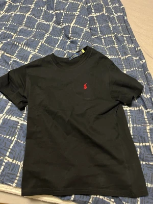 Polo Ralph lauren t shirt  - Klassisk svart t-shirt från Ralph Lauren med den ikoniska röda logotypen broderad på bröstet. T-shirten har rund hals och korta ärmar, perfekt för en enkel och stilren look.