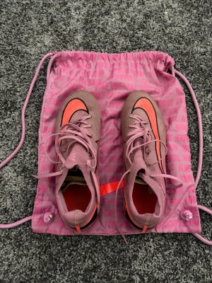 Nike rosa Mercurial fotbollsskor - Säljer ett par Nike Mercurial fotbollsskor i rosa med svarta och orange detaljer. Skorna har snörning, låg profil. Finns en liten defekt på skon som visas på sista bilden‼️pris kan diskuteras 