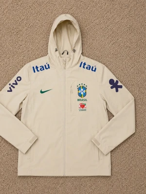 Vit Nike Brasil jacka med huva - Säljer en vit Nike jacka med huva, officiell Brasilien landslagsmodell. Jackan har dragkedja, flera sponsorloggor och Brasil-märket på bröstet. Tillverkad i lätt material, perfekt för träning eller sportiga dagar.