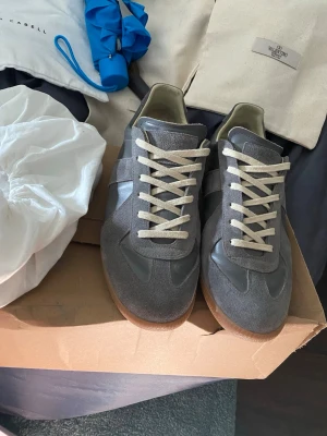 Maison Margiela Gats strl 41 grå - Säljer nu ett par Maison Margiela Gats i denna sällsynta grå färgen. Skorna är i storlek 41 men jag tycker de är ganska så rymliga (41-42). Dessa har gått igenom äkthetsverifiering och det tillkommer en lapp som bekräftar det vid köp, vilket ni kan se på sista bilden. Dessa är ett av få par som faktiskt är ÄKTA här på Plick. Skicket är mycket bra, de är lite använda, vilket ni ser på bilderna. De som tillkommer är dessutom två dustbags, tyvärr ingen box. Hör av er vid frågor och funderingar!