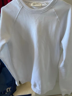 Vit sweatshirt från Pier One - En stilren vit sweatshirt från Pier One med rund halsringning och raglanärmar. Tröjan har ribbade muddar vid ärmslut och nederkant, perfekt för en clean och avslappnad look. Tillverkad i mjukt material som känns skönt mot huden.